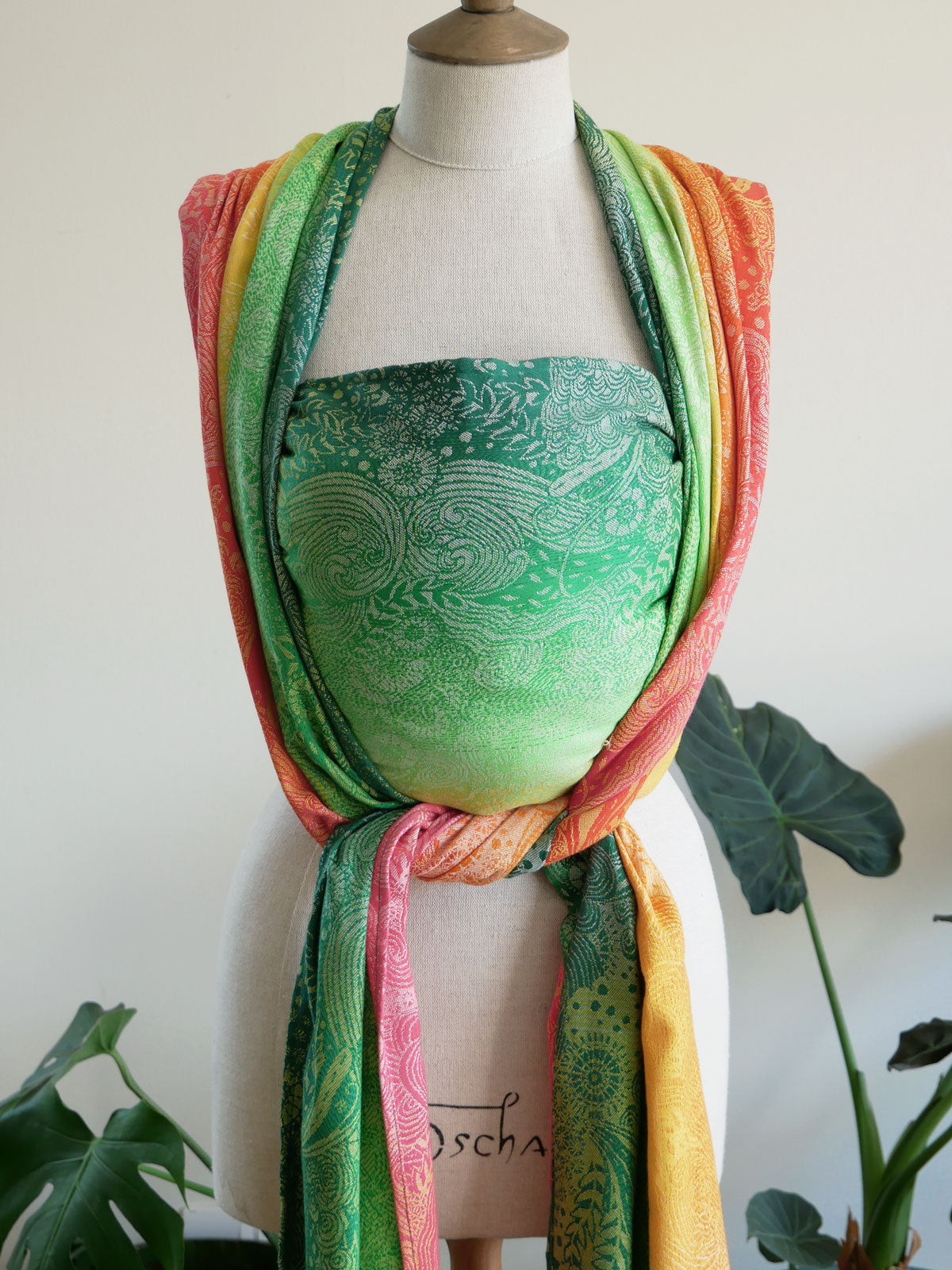 Mannequin wearing a colorful Marina Starburst Baby Wrap and green patterned top with a white background