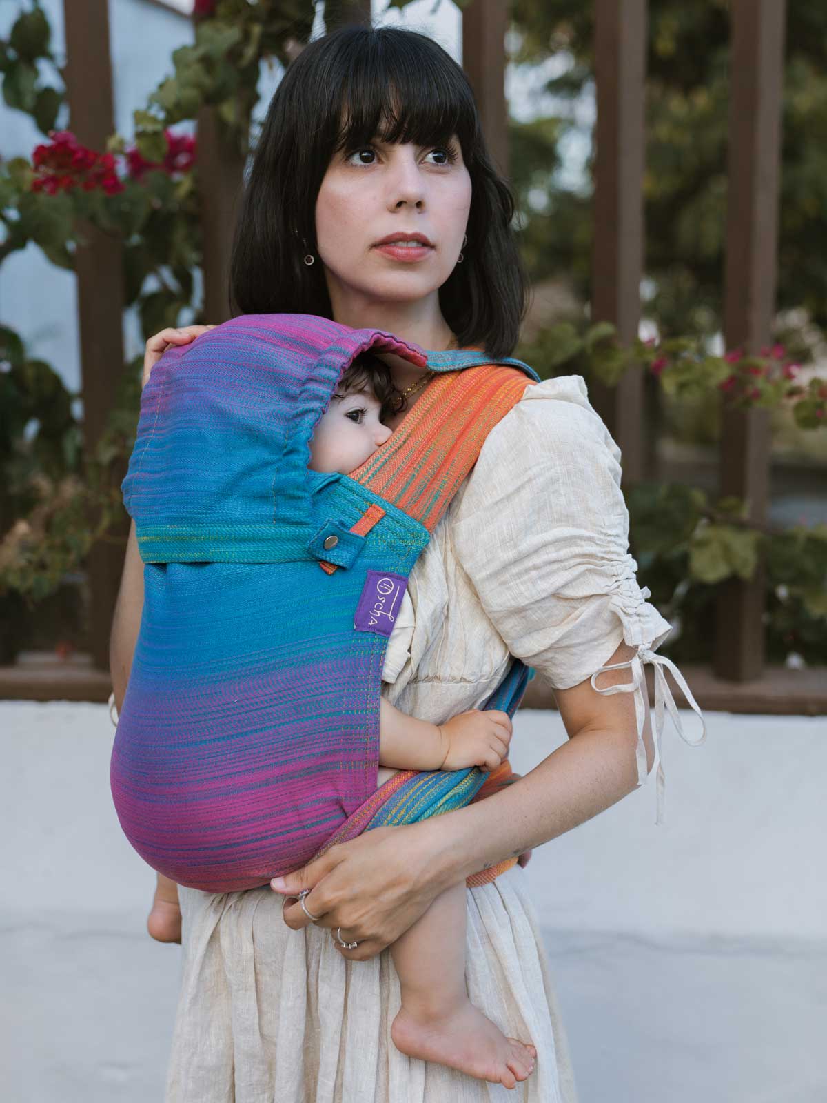 Mother holding a child in a baby carrier with hood. 