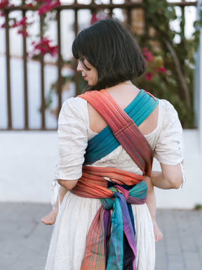 Back view of model using a baby carrier with crossed straps and knotted at the waist. 