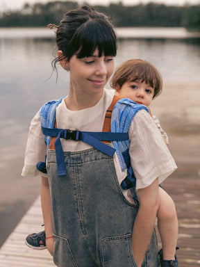Front view of a child in a blue Onbuhimo on a woman's back.
