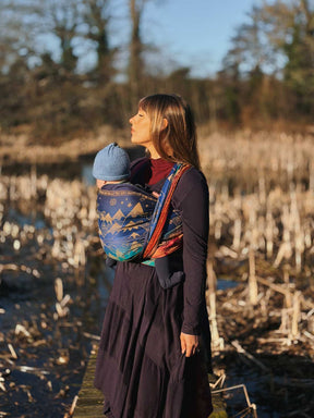 Woman carrying a child in a baby carrier through a natural landscape