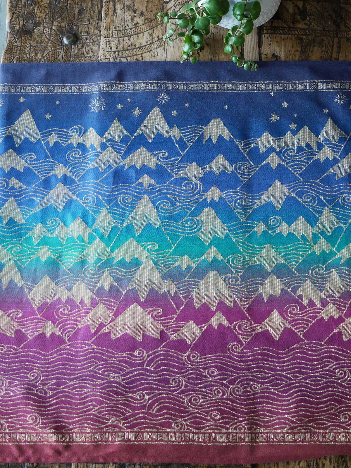 Textile with mountain pattern in blue, pink, and green on a wooden surface.