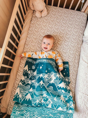 Baby lying in a crib with a patterned blanket and teddy bear