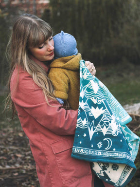 Woman holding a child wrapped in a teal blanket with white patterns outdoors.