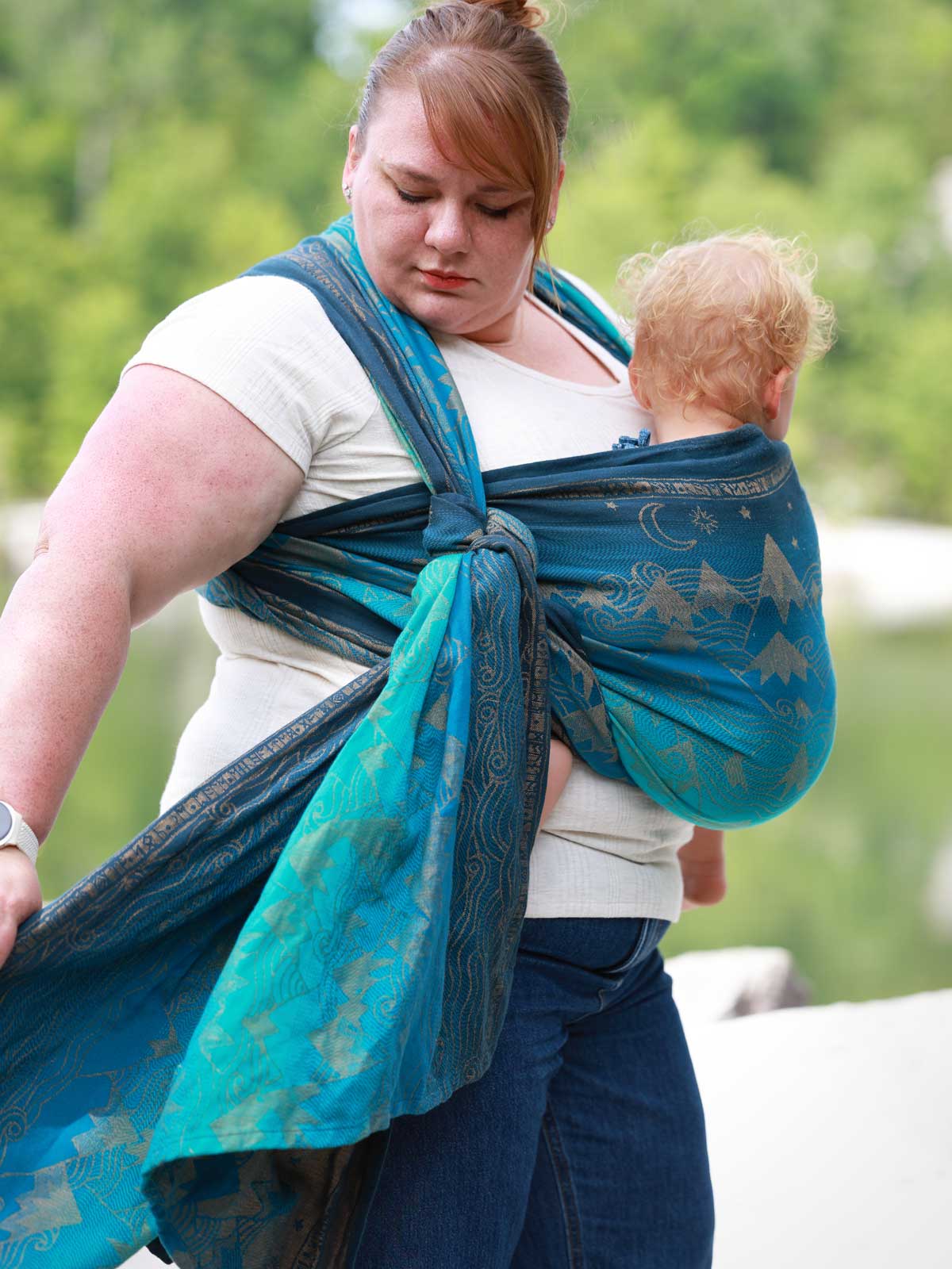 Woman carrying a baby in a blue teal woven wrap with a mountain pattern