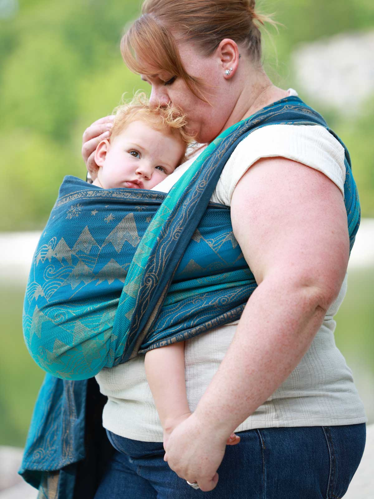 Woman carrying a baby in a blue teal woven wrap with a mountain pattern