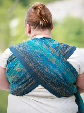 The back of a woman in a blue teal woven wrap with a mountain pattern