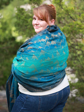 Model wears shawl in shades of teal with golden Misty Mountain pattern.