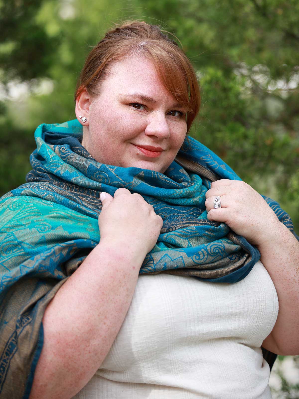 Model wears shawl like a scarf with teal and gold fabric. 