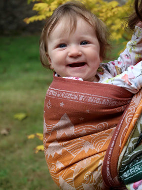 Baby smiling in a patterned wrap outdoors