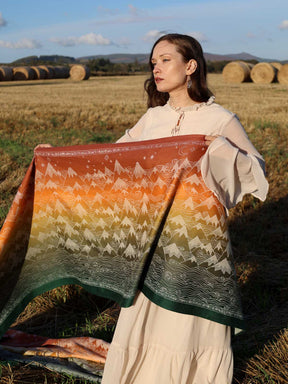 Woman holding a n autumnal coloured woven wrap in a field with hay bales.