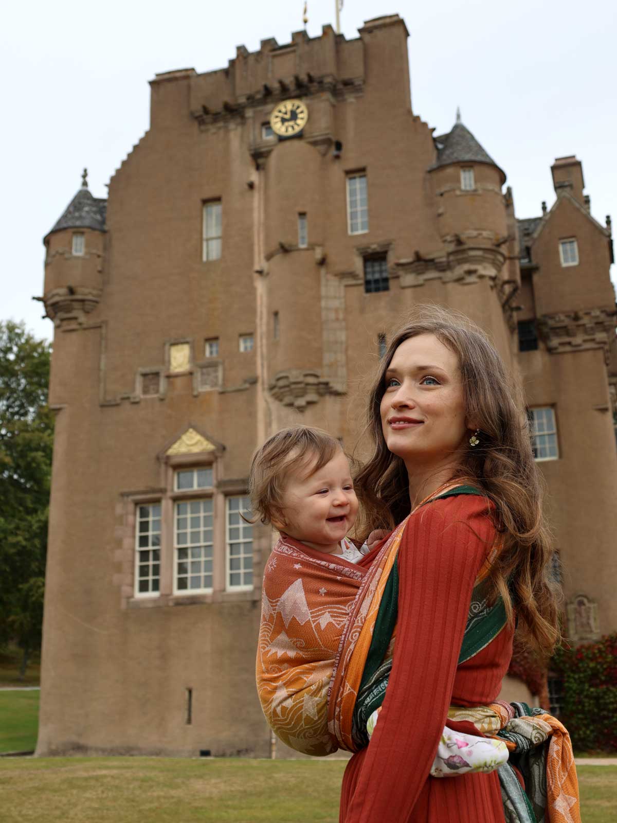 Woman carrying a child in a woven wrap in front of a castle