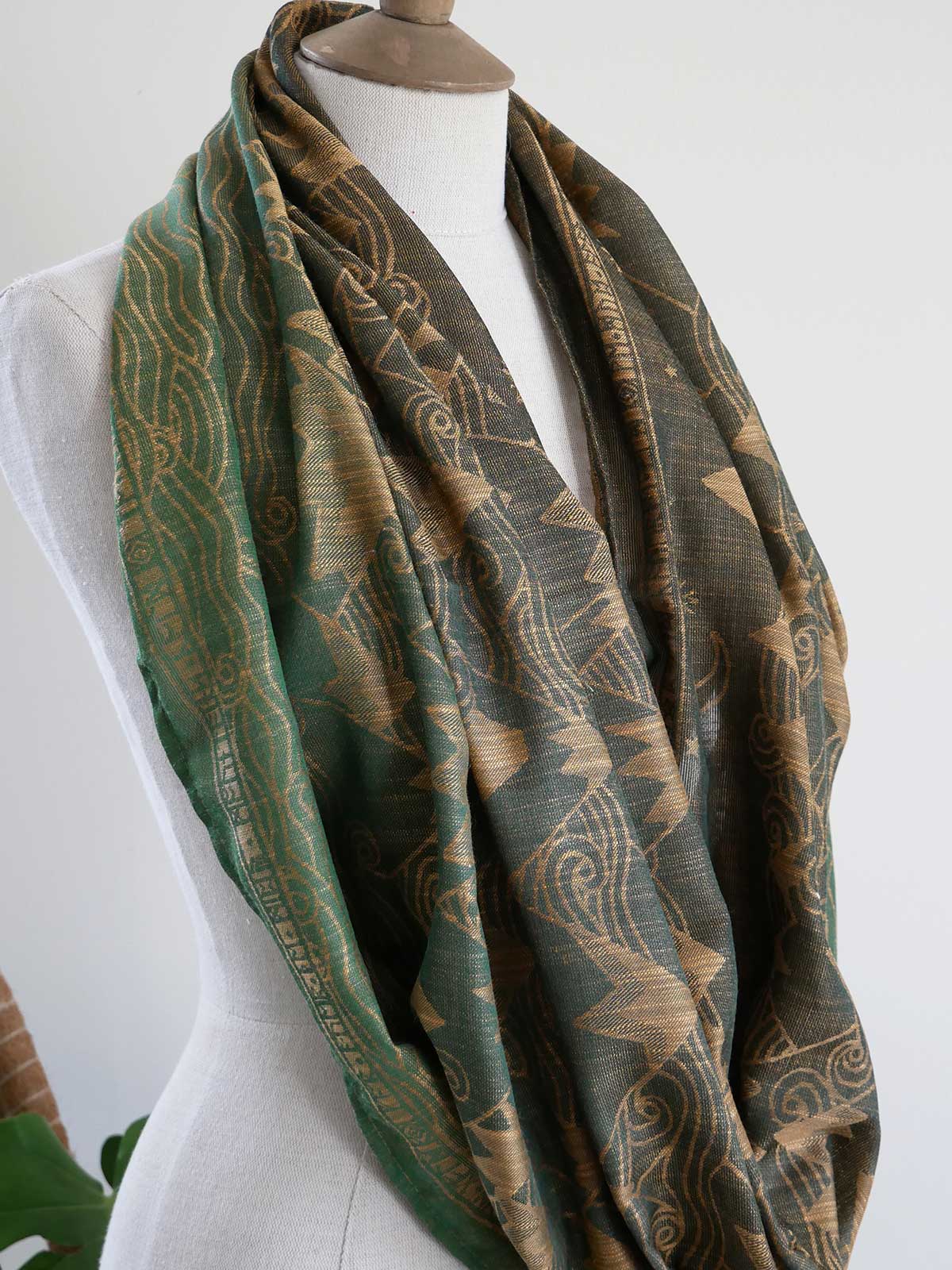Green and gold patterned scarf on a mannequin against a white background