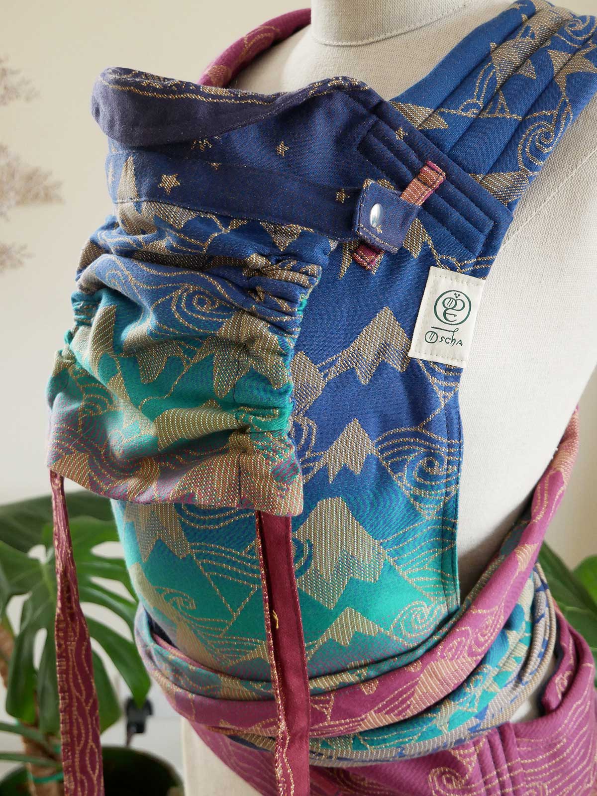 Colourful baby carrier with patterns on a mannequin against a neutral background