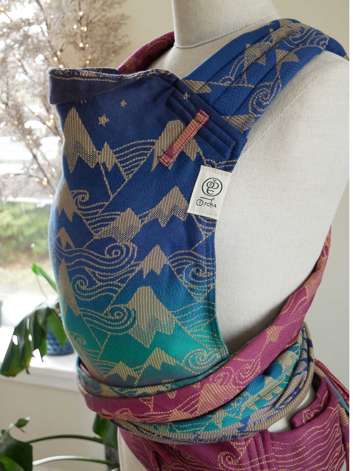 Colourful baby carrier with mountain design on a mannequin against a blurred indoor background