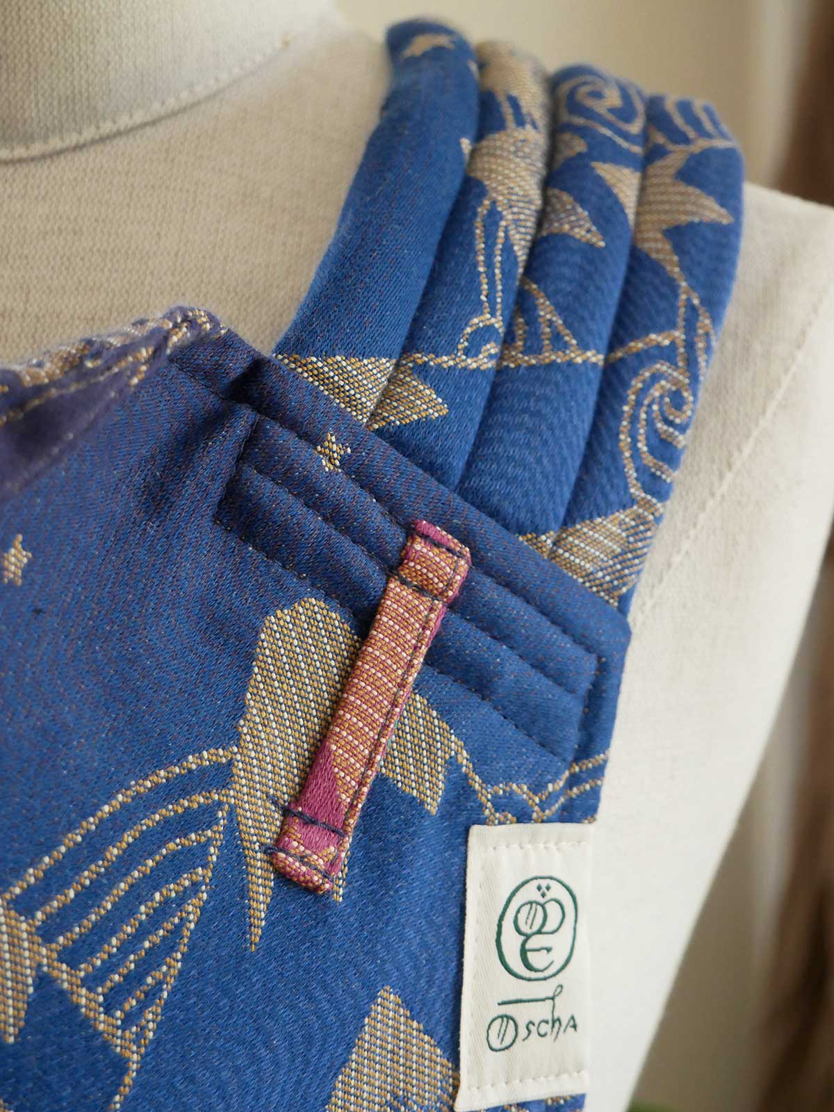 Blue fabric baby carrier strap with gold patterns on a mannequin, featuring a visible label.