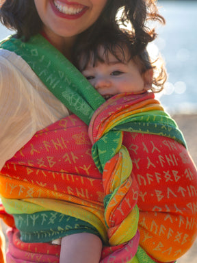 Child being carried in a colorful baby wrap with a blurred natural background