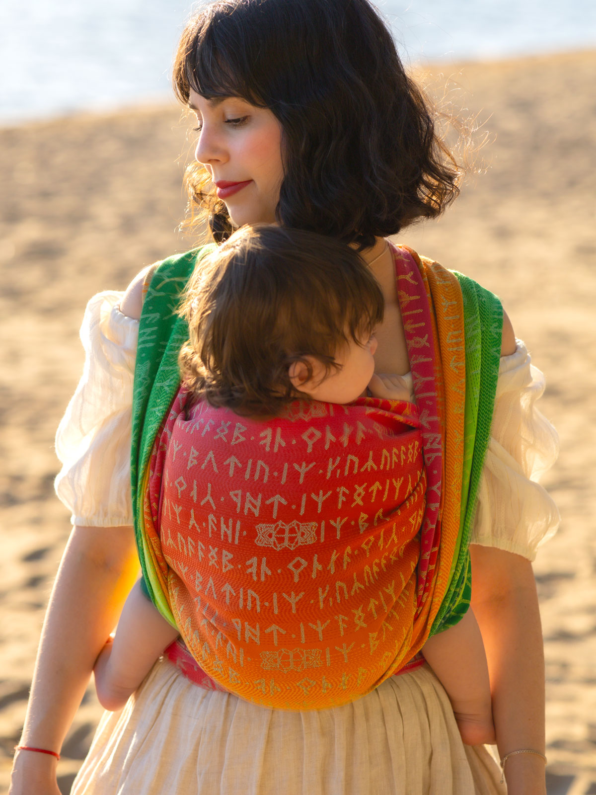 Woman carrying a child in a colorful Moria Citrus Baby Wrap outdoors
