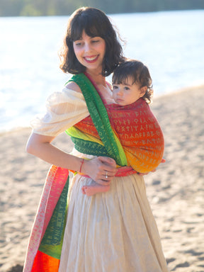 Woman holding a child on a beach with a colourful Moria Citrus Baby Wrap