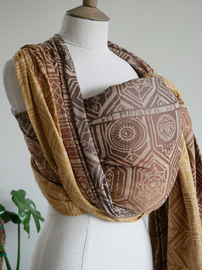 Mannequin wearing a patterned brown and gold woven wrap with a geometric design.