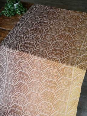 Hexagonal patterned fabric on a wooden table with a plant in the corner.