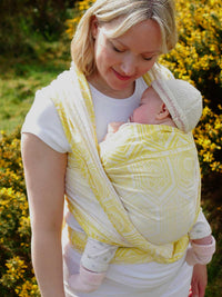 Woman wearing a baby in a yellow woven wrap with geometric pattern