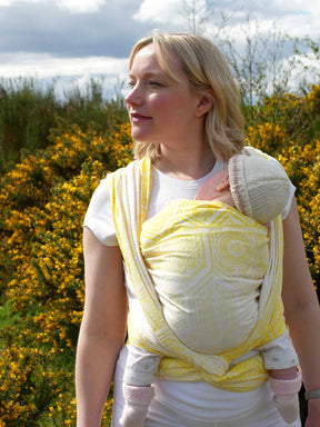 Woman wearing a baby in a yellow woven wrap with geometric pattern