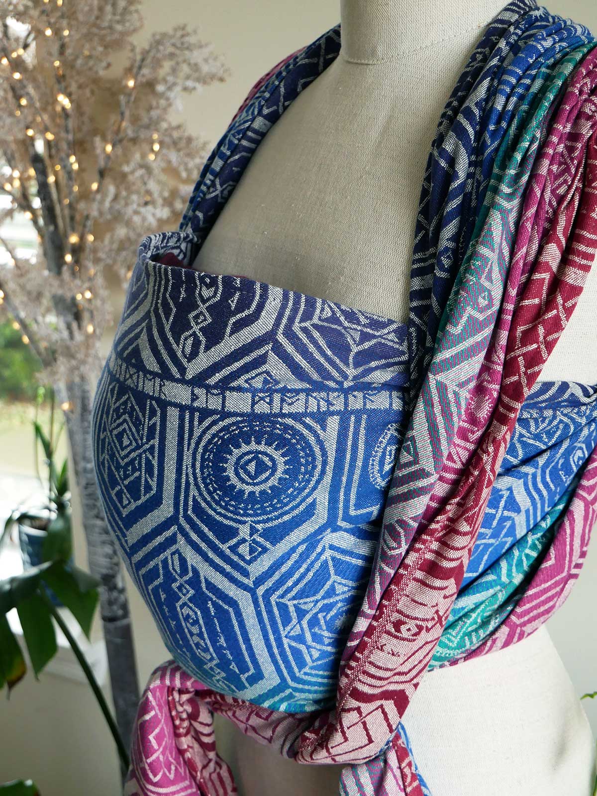 The side of Oakenshield Loden baby wrap on a mannequin in jewel tones with a repeating shield pattern.
