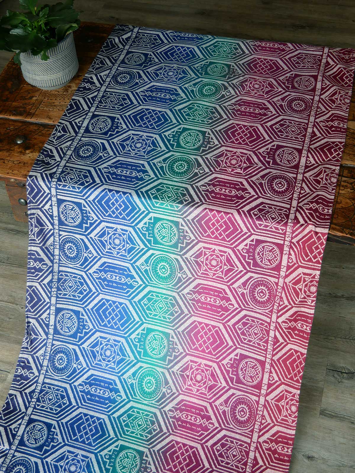 Fabric laid on a wooden table in jewel tones with a repeating shield pattern.
