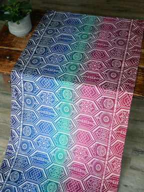 Fabric laid on a wooden table in jewel tones with a repeating shield pattern.