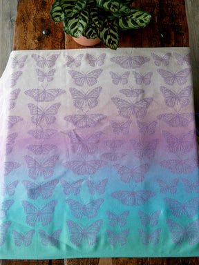 Butterfly patterned fabric with a gradient of purple to green on a wooden surface with a plant.