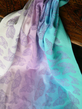 Gradient fabric with butterfly pattern transitioning from purple to green on a wooden surface.