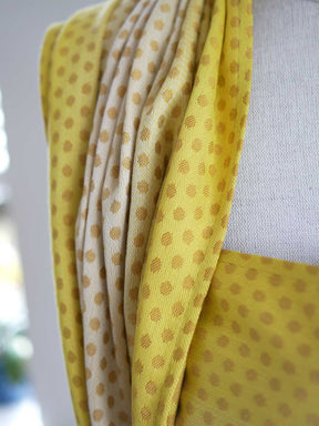 Close up of a lemon and gold woven wrap with dots on a mannequin.