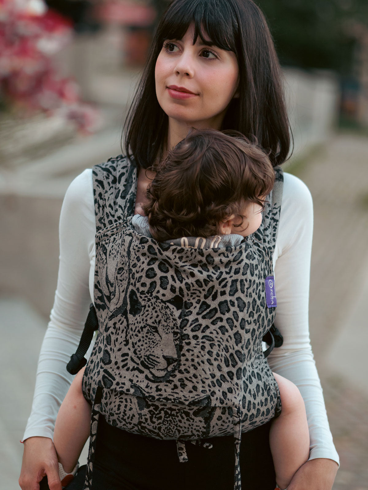 Woman carrying a child in a leopard print Prowl Savannah Bairn Baby Carrier outdoors.
