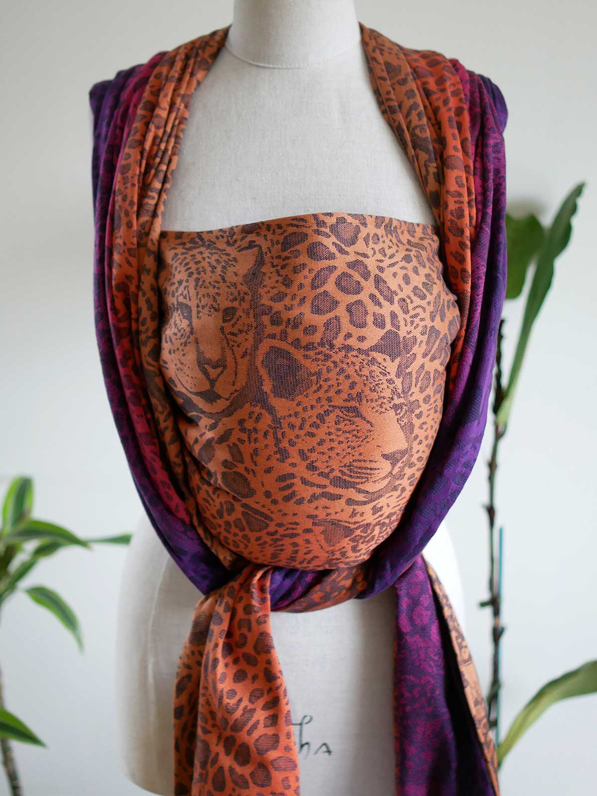 Front view of a leopard-print  woven wrap in orange, pink and purple with leopard faces, on a mannequin.