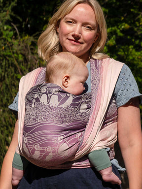 Front view of a woman wearing a baby in a pink and purple woveen wrap with puffin pattern
