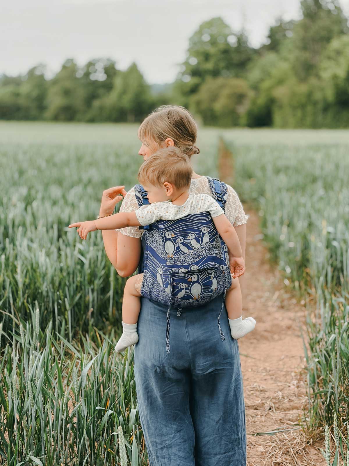 Model in grassy field carrying baby on back. 