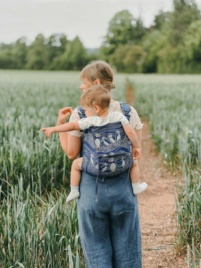 Model in grassy field carrying baby on back. 