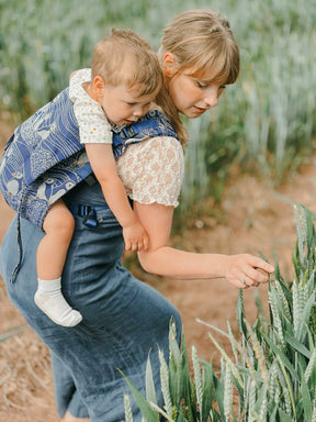 Model and baby in carrier looking at long grass. 