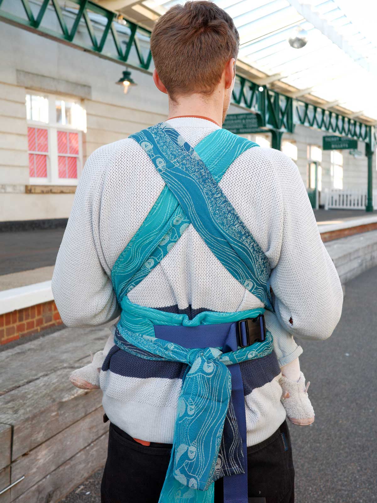 Person wearing a blue baby carrier in an outdoor setting