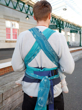 Person wearing a blue baby carrier in an outdoor setting