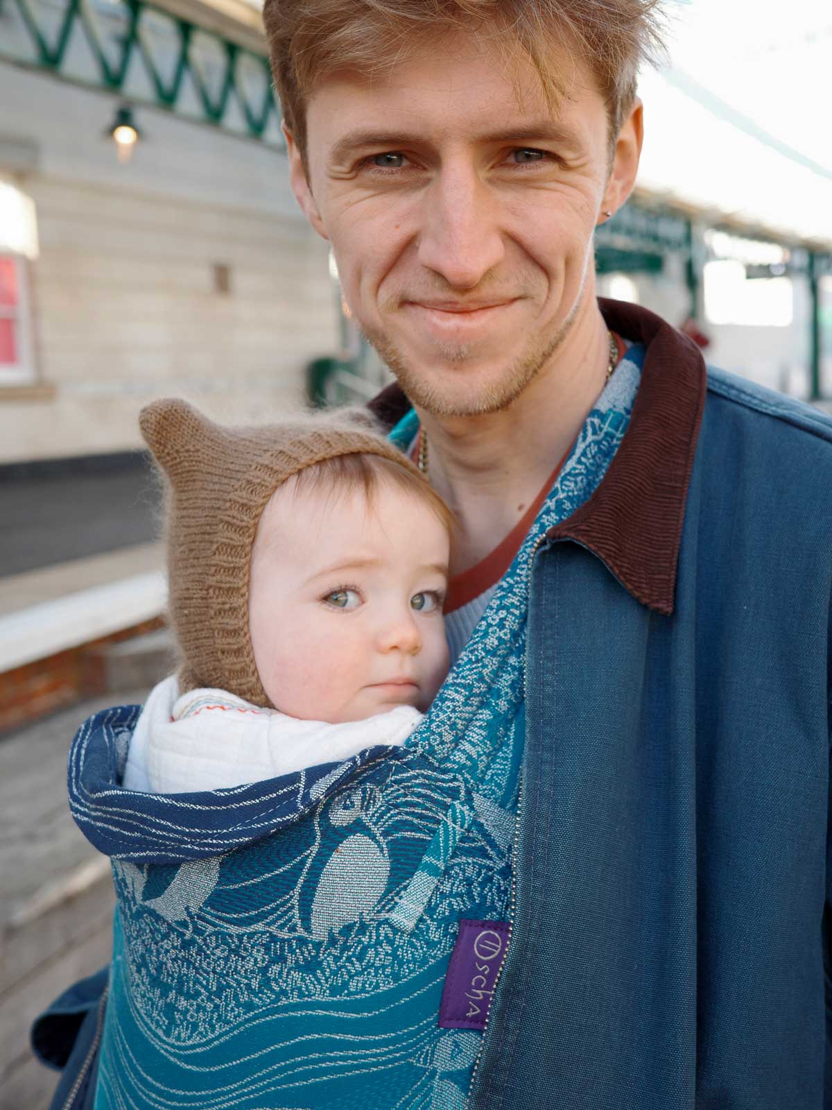 Man holding a baby in a blue carrier.