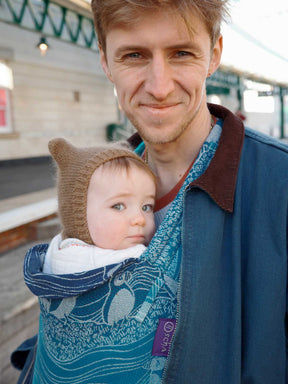 Man holding a baby in a blue carrier.