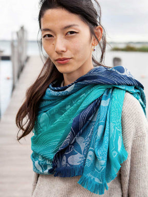 Close up of a  woman standing on a pier wearing a teal and blue scarf with puffin pattern