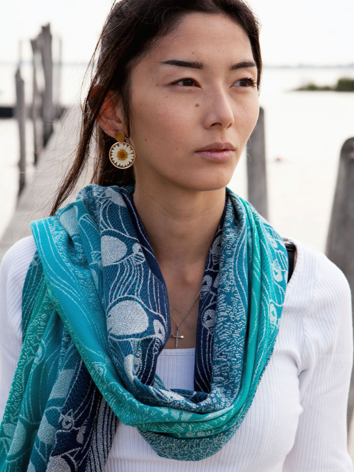 Woman wearing a teal shawl with a pattern, standing outdoors near water.