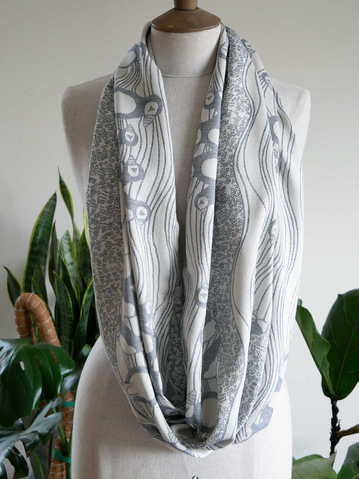 Gray and white patterned infinity scarf on a mannequin with a plant in the background