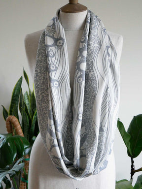 Gray and white patterned infinity scarf on a mannequin with a plant in the background