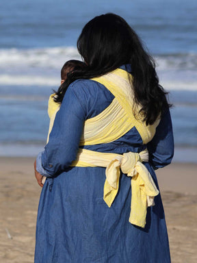 Woman with a baby in a yellow woven wrap on a beach