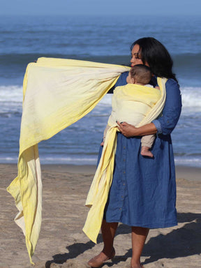 Woman putting a baby in a yellow woven wrap on a beach