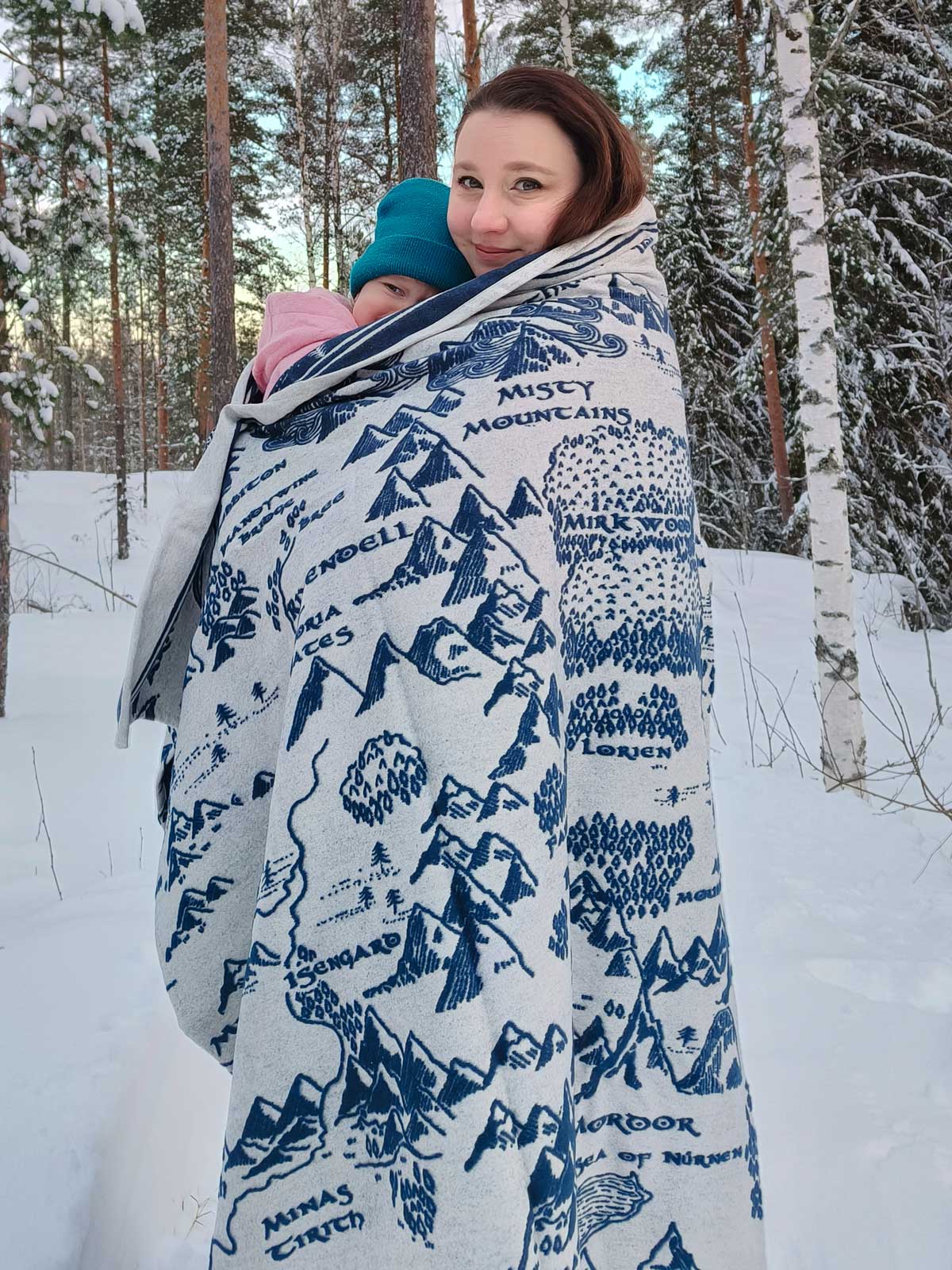Mum and baby wrapped in a The Lord of the Rings blanket with mountain patterns in a snowy forest.